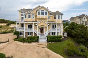 Beautiful yellow beach house with white trim near OBX beaches, featuring multiple balconies and a landscaped yard.
